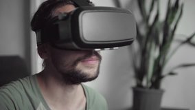 Young bearded hipster man using his VR headset display for virtual reality game or watching the 360 video and trying to touch to something he see while sitting on sofa. VR Technology.