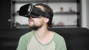 Young bearded hipster man using his VR headset display for virtual reality game or watching the 360 video while sitting on sofa at home in the living room. VR Technology.