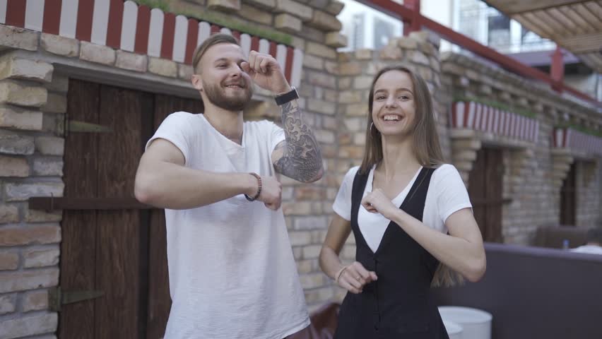 Happy and attractive young couple in love dance together in stylish summer bar. In slow motion.