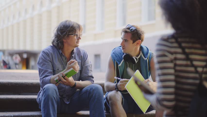 Professor helping his student with science project sitting on stairs outside. Male student and professor having conversation sitting on stairs.