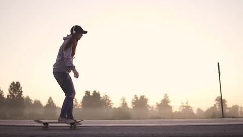 silhouette of a girl skating on a skateboard on a deserted highway at sunset. slow motion.