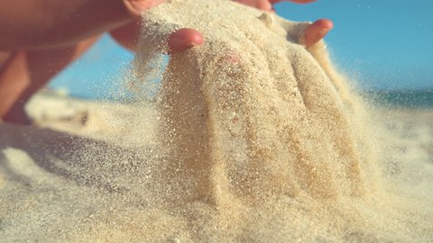 SLOW MOTION, CLOSE UP: Unknown playful young woman throws a handful of white sand over the camera. Carefree girl on summer holiday in Cook Islands plays on stunning tropical beach with soft sand.