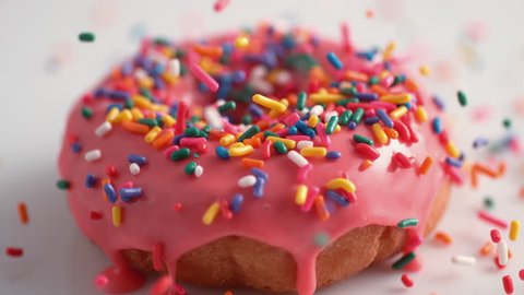 Sprinkling candy chocolate on frosted doughnut. Shot with high speed camera, 4K. Slow Motion.