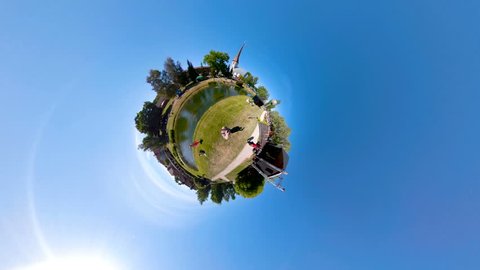 A panoramic little planet scene of the people in the park playing with the zorb ball with the trees on the side