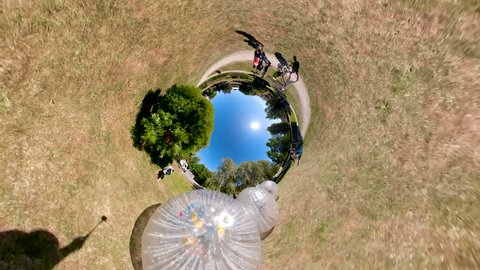 The panoramic little planet view of the three zorb balls in an open park on a sunny day