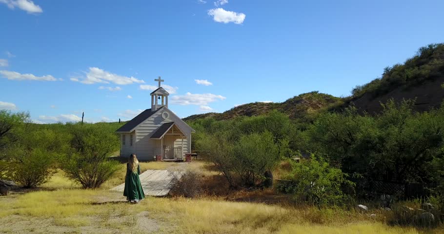 Western women walks to church while drone flies over head.