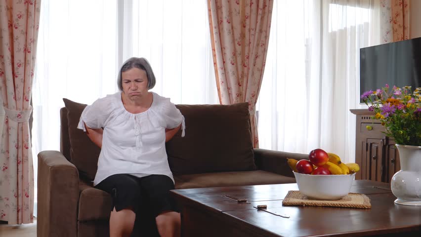 Mature woman suffering from backache at home. Massaging lower back with hands, feeling exhausted, standing in living room. Slow motion 4k | Shutterstock HD Video #1015543855