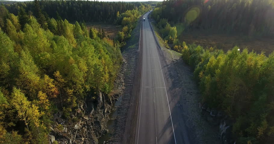 Aerial view at northern asphalt highway in autumn coniferous forest and mountain passage. Drone flying back