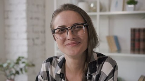 Portrait of business owner female model looking to the camera and smiling. Young professional saleswoman having photosession in home interiors. Woman wearing glasses and casual shirt for this work 