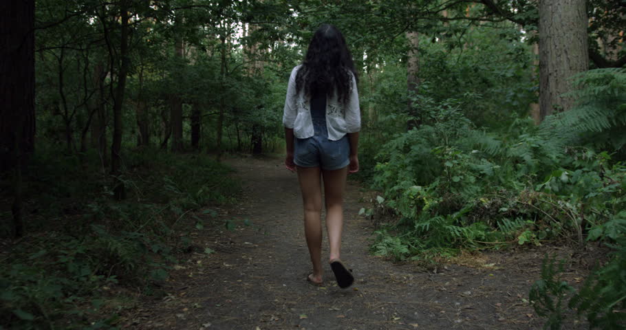 A Pretty Mix Race Young Student Girl Exploring The Woods on A Summers Day. Wearing Denim Dungarees and White Summer Shirt. Walking Through the Tall Trees Looking Around. Having Fun.