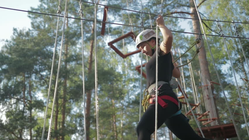 Young beautiful brunette overcomes obstacles in the rope town. A girl with a white helmet on her head and protective gear is on the track Royalty-Free Stock Footage #1015555810