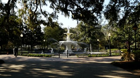 Wide shot of the water fountain and walkway in Forsyth Park, Savannah Georgia USA.  Framed by the live oak trees filled with Spanish Moss.  The water spray is lit by the early morning / evening sun.