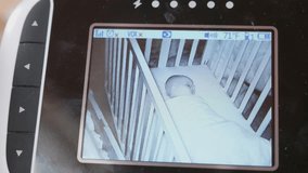 A dolly shot of a baby monitor with a cute newborn baby girl sleeping in her crib
