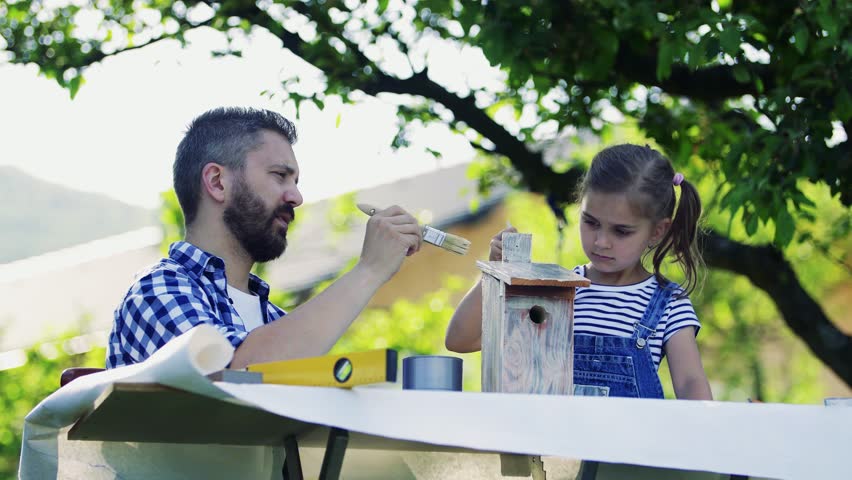 Father with a small daughter outside, painting wooden birdhouse.