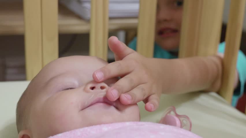 A newborn baby girl is very happy to have her older brother play with her in her crib
