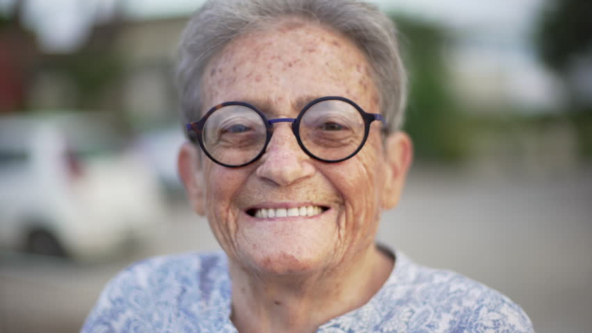 Portrait of happy elderly woman with black round glasses looking at camera and smiling with white teeth. | Shutterstock HD Video #1015558867