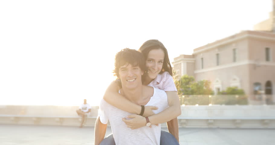 Two beautiful teenager friends or young couple having fun together, giving her piggyback rides, in the city in spring or summer. Young boy and girls amuse themselves in the town.