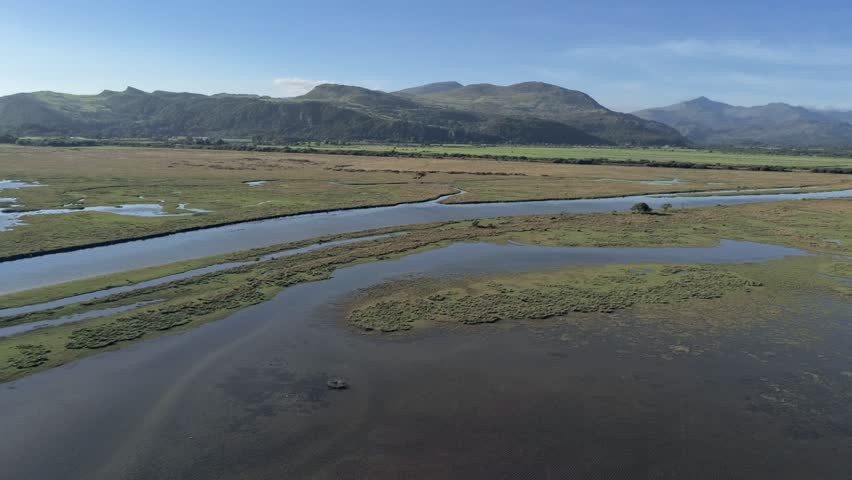 Aerial view, down move. Drone panorama over Glaslyn reserve wetlands, water and mountains in background in sunny Wales