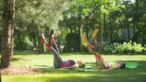 Sporty women training abs workout doing scissors lifts leg raise exercise while lying on fitness mats on grass in park. Fit females practicing legs scissors abdominal abs exercise outdoors. Slo mo. 스톡 비디오