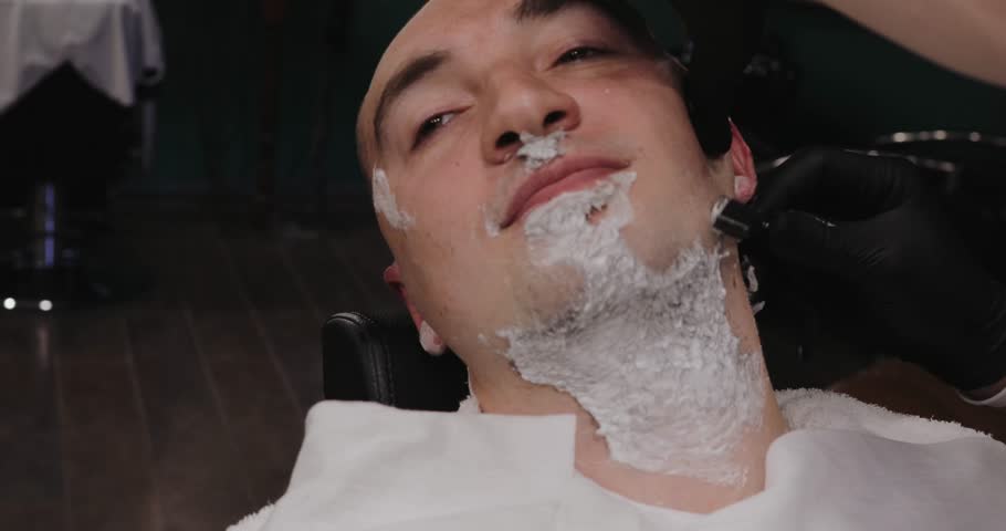 Barber shaves beard of men in the barbershop, shaving cream on bristles | Shutterstock HD Video #1015566979