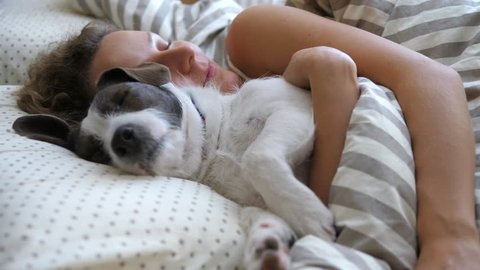 Girl And Her Pet Dog Hugging In The Bed.