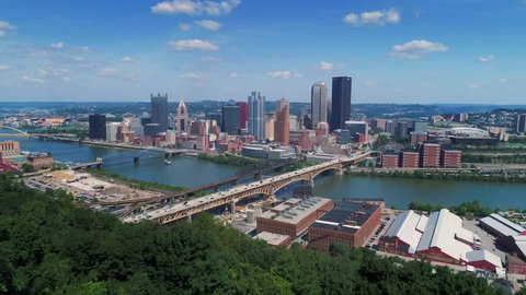 A rising wide aerial establishing shot of the iconic Pittsburgh, Pennsylvania skyline on a summer day as seen from Emerald View Park. Monongahela River in the distance.	