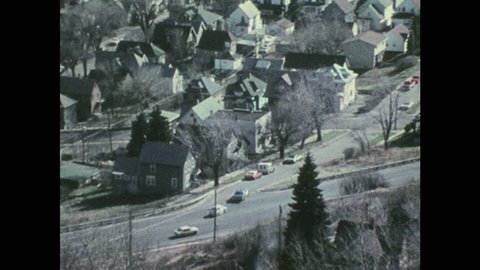 1970s: UNITED STATES: overhead view of police car driving along road in town. View across settlement from above