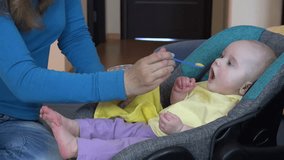 Playful woman feeding cute hungry baby with mash in green spoon. Mother put maize mash in infant child mouth at home. 4K UHD video clip.