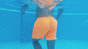 A young guy swims underwater in a swimming pool on a blue background. Underwater video.