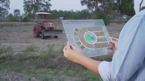 Asian female farmer using portable tablet computer to inspect the agricultural engine in farmland. Modern hologram farming concept, advanced technology in agriculture.