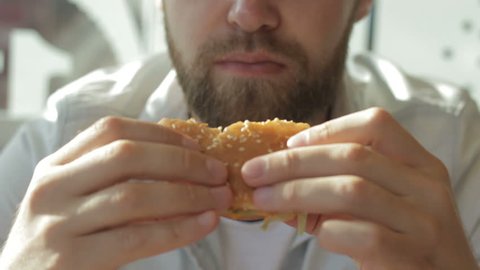 Handsome lonely, addicted bearded guy having breakfast in fast food restaurant