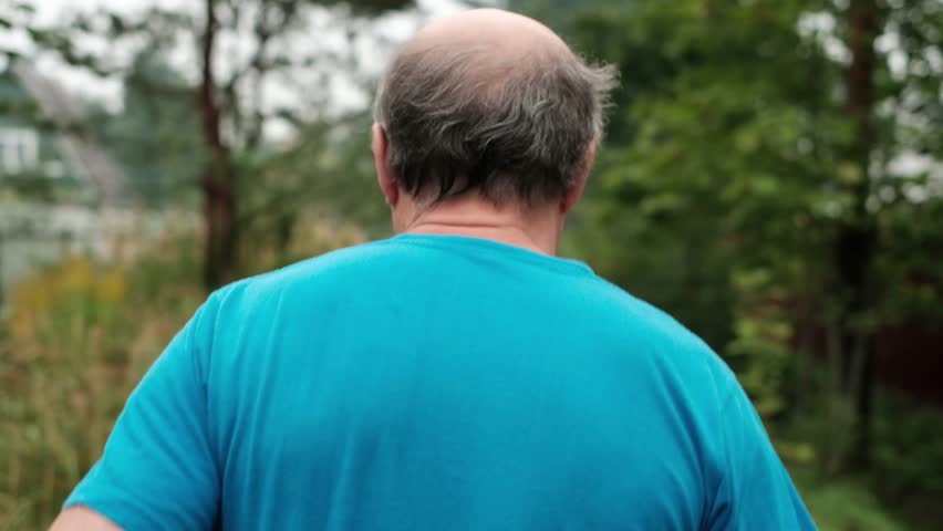 Mature man running on road through trees. Back view. Senior male having active lifetyle during summer vacation in Russia