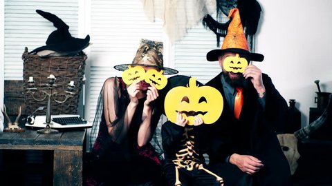Halloween party and celebration concept. Wizard, witch and the little skeleton hide their faces behind pumpkins. Family in costumes have fun on halloween