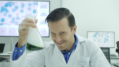 Portrait of Crazy and mad scientist laughing and holding volumetric flask with green liquid in laboratory.