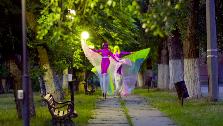 Two beautiful girls on stilts walk away at the street