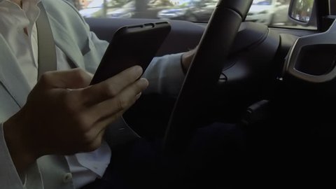 Male driver texting message. Closeup of smartphone in hand. Unidentified business man using phone while driving car. Traffic violation and careless driving concept