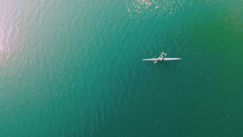 Wonderful aerial footage of man swimming in kayak on blue river water. Drone view. Floating alone on the lake in canoe. Sports activity, adventure concept.