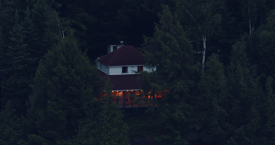 Aerial shot of old cottage and wood shed at evening sunset with string lights on screened in porch