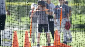 Slow motion shot of kid pitching ball towards net during baseball practice. Other kids and coach are standing around him. - Powered by Shutterstock - Get 15% off with code: PIKWIZARD15