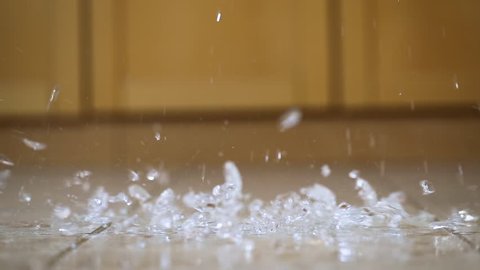 Glass of water hitting the ground shattering and splashing on the kitchen floor, slow motion 120 FPS capture