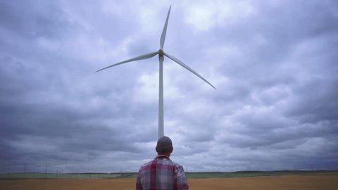 Man on field walking toward large wind turbine near Fort Macleod, Alberta, Canada