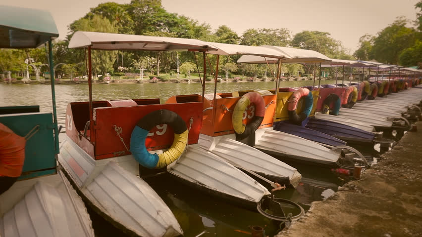 Colorful pedal boats parked in a long line at pier in park.  Processed with vintage style.