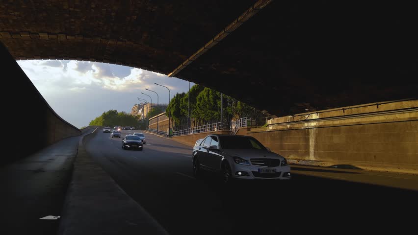 Traffic flowing through a tunnel next to the Seine in Paris, France during sunset. Motorbikes, scooters, taxi and different cars can be seen. On the left is a bike lane where a couple of bikes appear.