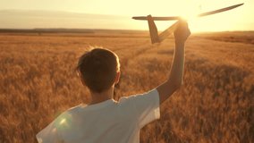 Happy kid run with toy airplane at sunset over wheat field. Kid dreams of becoming an astronaut pilot. Airplane pilot. Children dream to run with toy. Kid airplane pilot. Dream concept. Wheat field
