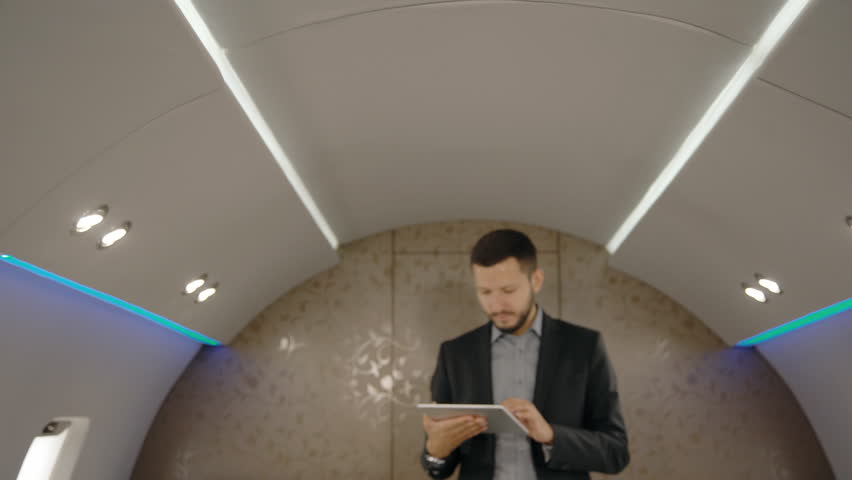 Portrait of chief banker director man standing in plane and lookins to the screen of his tablet. Concept of: business people, plane flying, tablet reading.