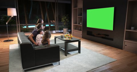 A family is watching a TV and celebrating some joyful moment, sitting on the couch in the living room. The living room is made in 3D. TV is green screen for further editing.