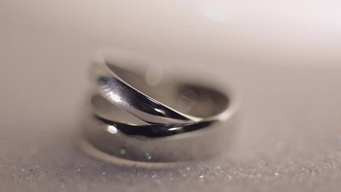 Wedding silver rings lying on shiny shining surface with light, close-up macro footage. Rotate spinning clockwise. Pair of marriage symbols. Love of bride and groom, wife and husband. Matrimony symbol