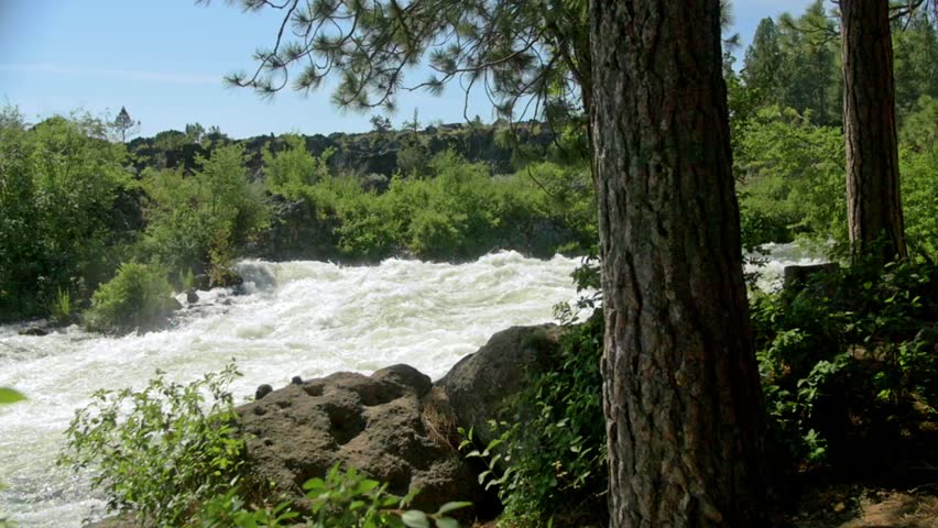 Panning shot of a group of white water rafters floating down a babbling river in Bend, Oregon