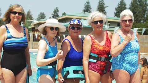 Five adorable old ladies wearing festive bathing suits and sunglasses stand by the pool, and flex their muscles at the camera