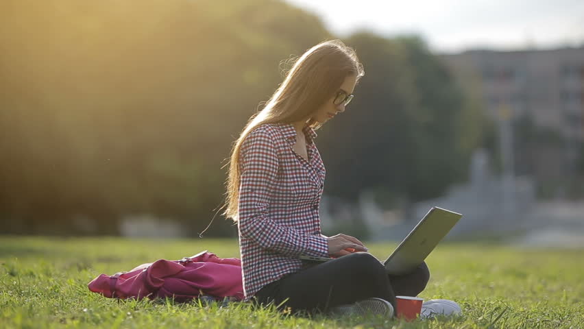 Busy attractive girl working at the laptop as sitting on grass in city park on hectic summer morning, outdoor shot in urban area Royalty-Free Stock Footage #1015666522